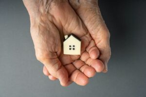 Inheritance,Concept.,Elderly,Woman,Hands,Holds,A,Little,Toy,House.